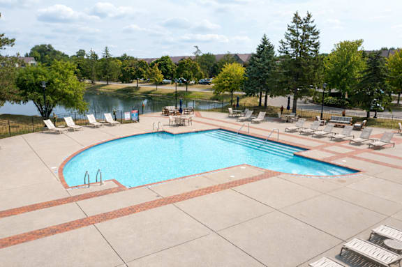A large outdoor swimming pool surrounded by lounge chairs and trees.