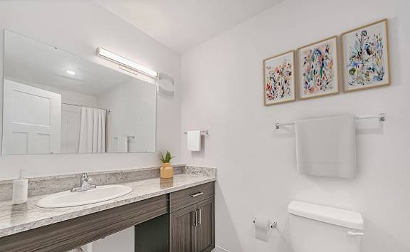 A bathroom with a sink, toilet, and a mirror at Strathmore Apartment Homes in West Des Moines, IA
