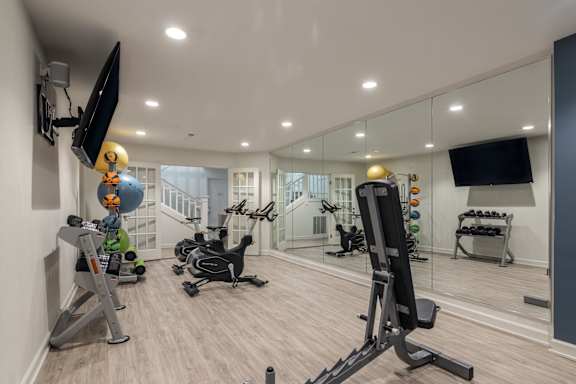 A well-equipped home gym with various exercise machines and a flat-screen TV mounted on the wall.