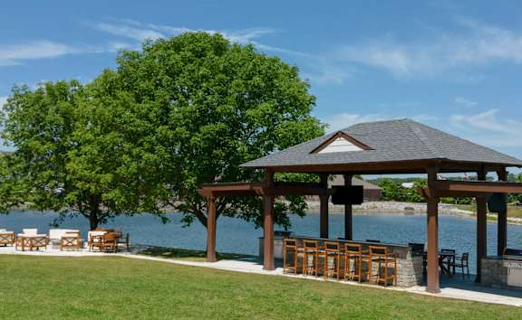 A gazebo with a table and chairs is situated on a lawn by a body of water.