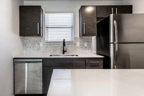 A modern kitchen with a stainless steel refrigerator and a marble backsplash.