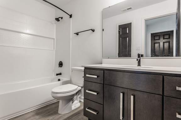 A white toilet sits in a bathroom with a wooden vanity and a large mirror.