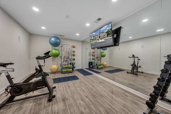A home gym with a variety of exercise equipment including a stationary bike, a treadmill, and a television mounted on the wall. at Sunscape Apartments, Roanoke