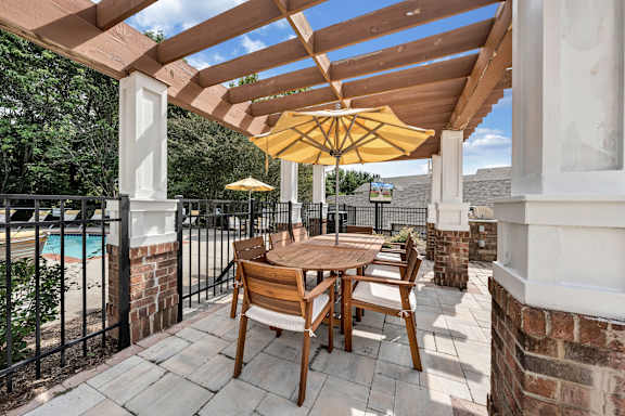 A wooden table and chairs are set up on a patio with a yellow umbrella. at Sunscape Apartments, Virginia