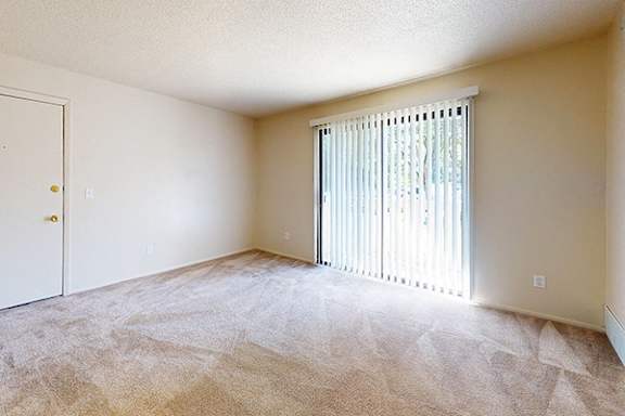 A carpeted living room leading to a private patio at Swiss Valley Apartments in Wyoming, MI