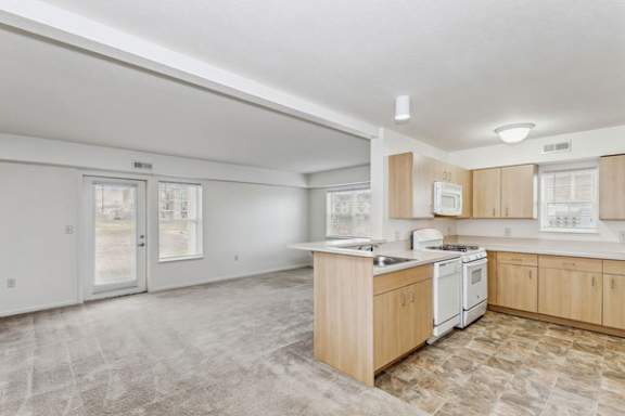 A kitchen with white appliances and an enlarged living room at Tall Oaks Apartment Homes, Kalamazoo, MI, 49009