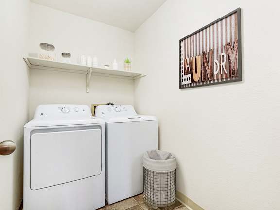 A laundry room with a washer and dryer and a shelf  at Tanglewood Apartments, Oak Creek, WI