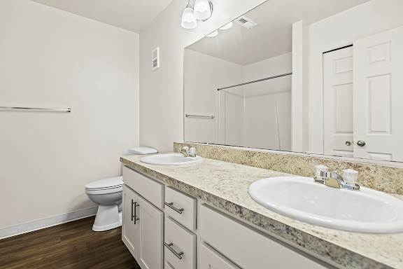 An ensuite bathroom with a toilet, two sinks, and mirror at Tanglewood Apartments, Oak Creek, WI