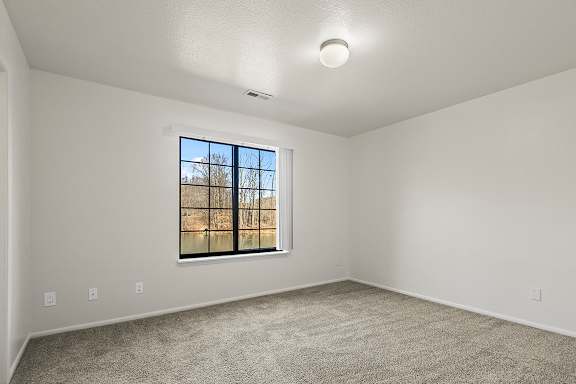 A bedroom with a large window and a carpeted floor at Tanglewood Apartments, Oak Creek, WI