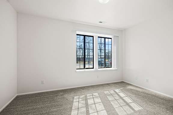 A spacious bedroom with a large window and a carpeted floor at Tanglewood Apartments, Oak Creek, WI