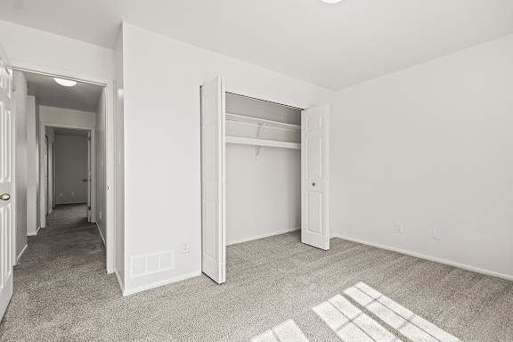 A bedroom with a carpeted floor and a white closet at Tanglewood Apartments, Oak Creek, WI