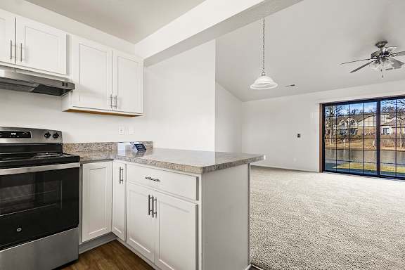 A kitchen with white cabinets and a breakfast bar leading to a living room at Tanglewood Apartments, Oak Creek, WI
