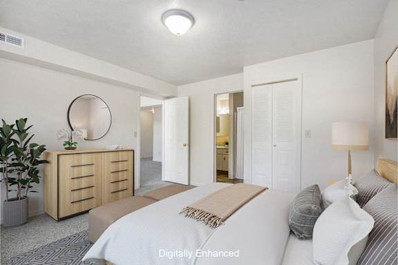 A bedroom with an ensuite, a bed, nightstand, and a plant at The Highlands Apartments, Elkhart