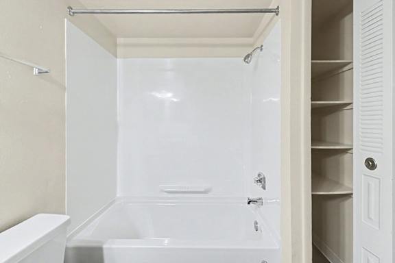 A white bathroom with a tub, shower and linen closet at Trappers Cove Apartments, Lansing
