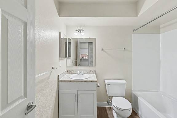 A white bathroom with a toilet, sink, and bathtub at Trappers Cove Apartments, Lansing