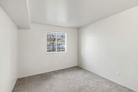A bedroom with a large window and a carpeted floor at Trappers Cove Apartments, Lansing