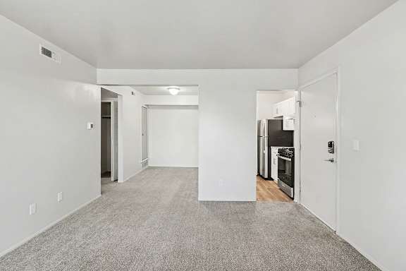 A spacious living and dining room with a carpeted floor and white walls at Trappers Cove Apartments, Lansing