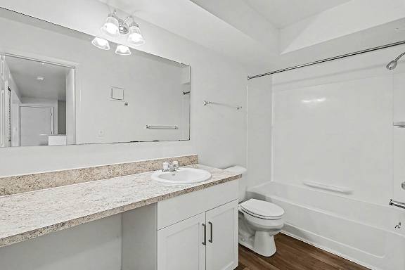A white bathroom with a sink, mirror, and bathtub at Trappers Cove Apartments, Lansing