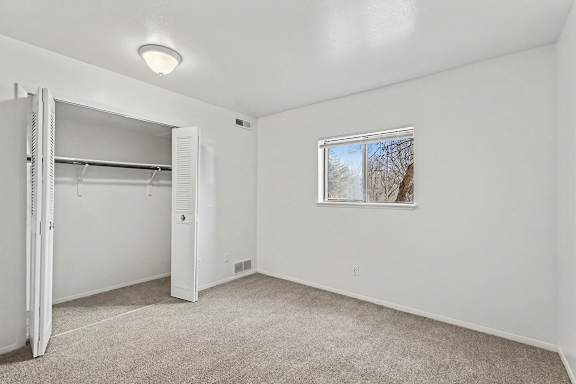A white bedroom with a window and a large closet at Trappers Cove Apartments, Lansing