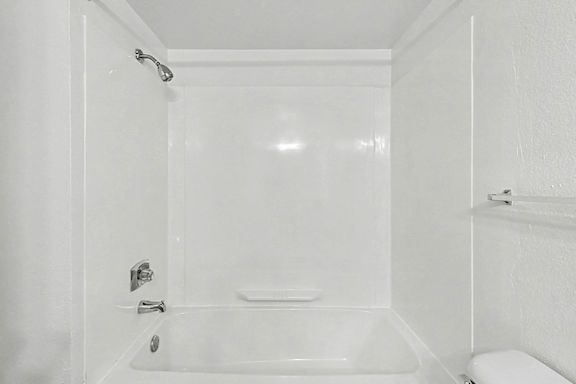 A white bathroom with a tub and toilet at Trappers Cove Apartments, Lansing