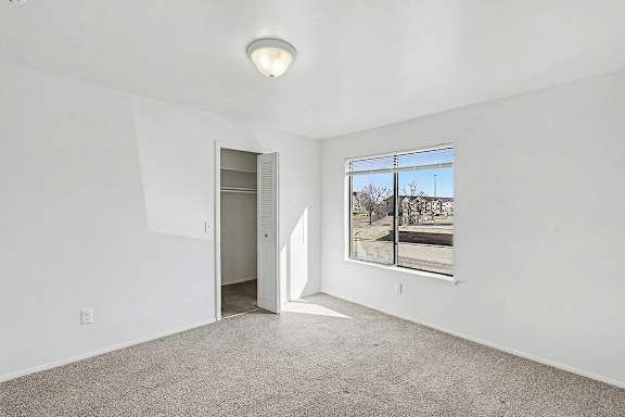 A bedroom with a carpeted floor, a large window, and a closet at Trappers Cove Apartments, Lansing