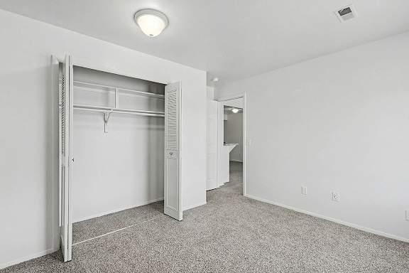 A white bedroom with a closet and plush carpeting at Trappers Cove Apartments, Lansing