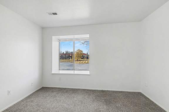 A bedroom with a large window showing a pond view at Trappers Cove Apartments, Lansing