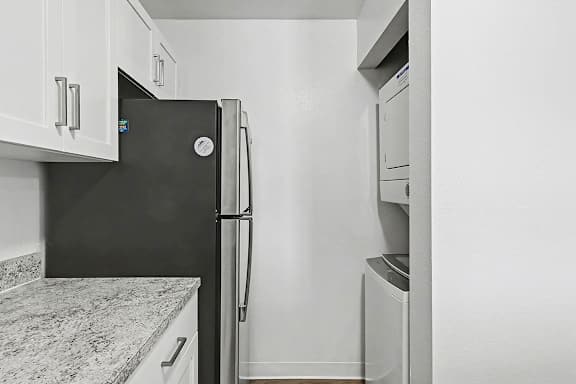A kitchen with white cabinets and a washer and dryer at Trappers Cove Apartments, Lansing