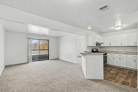 A spacious kitchen and living room with white cabinets and a slider to a balcony at Trappers Cove Apartments, Lansing