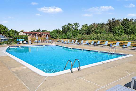 A large outdoor swimming pool with blue water and a metal ladder at Trappers Cove Apartments, Lansing, MI, 48910