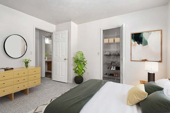 A bedroom with a bed, dresser, and a walk-in closet with wardrobe organizers at Trillium Pointe Apartment Homes, Jackson