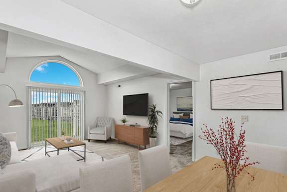 A living room with a television, a couch, a chair, a coffee table, and a bed in the background.