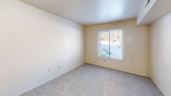 A bedroom with a large window and carpeted floor at Walnut Trail Apartments, Michigan