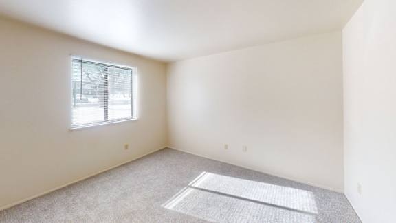 A bedroom with a window and plush carpeting at Walnut Trail Apartments, Michigan