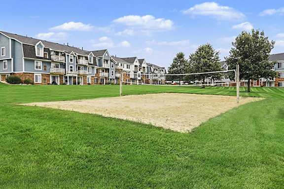 A volleyball net is set up on a sandy patch in the middle of a grassy area at Walnut Trail Apartments, Portage, MI