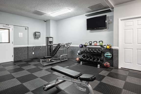 A gym with a bench, weights, and a television at WaterFront Apartments, Virginia Beach