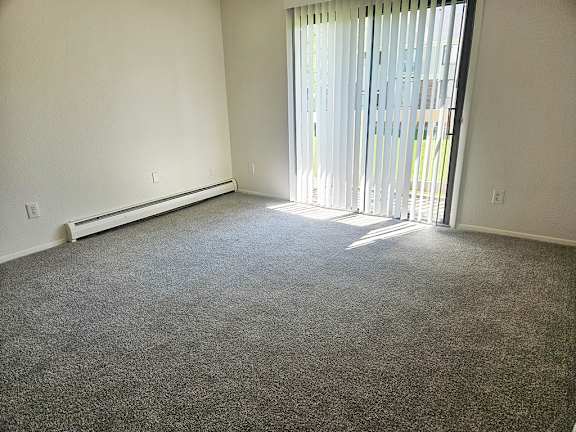 A living room with a carpeted floor and a slider to a patio with blinds at Waverly Park Apartments, Lansing