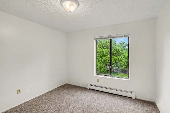 A bedroom with a large window and plush carpeting at Waverly Park Apartments, Lansing, Michigan