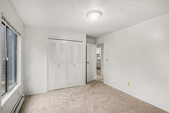 A bedroom with a window, closet doors, and a carpeted floor at Waverly Park Apartments, Lansing, Michigan