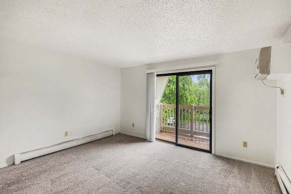 A living room with a carpeted floor and a sliding glass door leading to a balcony at Waverly Park Apartments, Lansing, Michigan