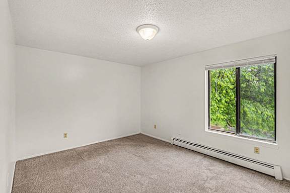A spacious bedroom with a window and a carpeted floor at Waverly Park Apartments, Lansing, MI