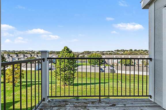 A balcony with a metal railing overlooks lush, green grounds at West Hampton Park Apartment Homes, Nebraska, 68022