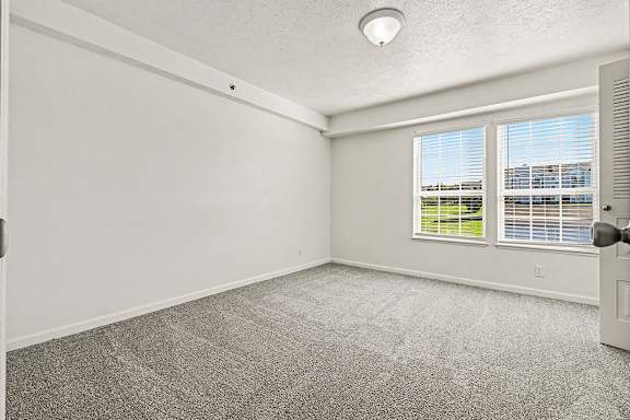 A spacious bedroom with a carpeted floor and a window showing a view of a building at West Hampton Park Apartment Homes, Nebraska, 68022