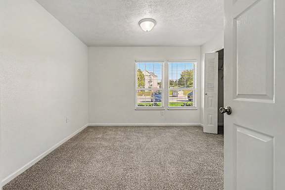 A bedroom with a large window, carpeted floor and a door leading to a walk-in closet at West Hampton Park Apartment Homes, Nebraska, 68022