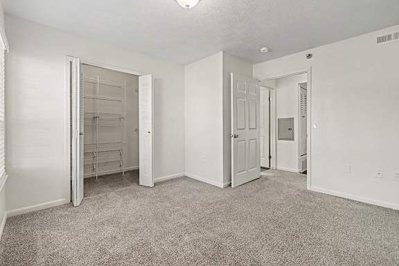 A white bedroom with a carpeted floor and a walk-in closet with organizers at West Hampton Park Apartment Homes, Nebraska, 68022