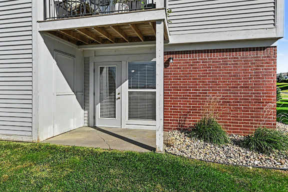 A patio with a white French door and enclosed storage at West Hampton Park Apartment Homes, Nebraska, 68022 a window with blinds.