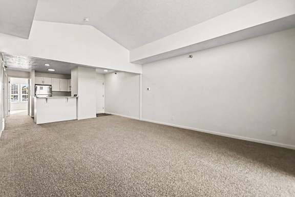A large, empty living and dining room with carpeted flooring and a cathedral ceiling at West Hampton Park Apartment Homes, Nebraska, 68022