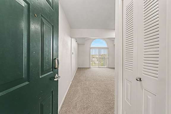 An entryway with a green door and a white closet door with a living room window in the distance at West Hampton Park Apartment Homes, Nebraska, 68022
