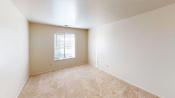 A bedroom with a large window and carpeted floor at West Wind Apartments in Fort Wayne, IN