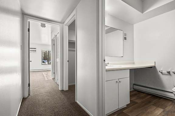 A hallway looking into a bathroom with a sink, mirror, and toilet at Wood Creek Apartments, Kenosha